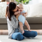 Mother sits on the living room floor and holds her happy baby.